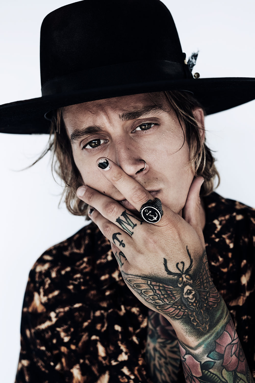 Studio portrait with a wide-brim black hat and tattooed hand